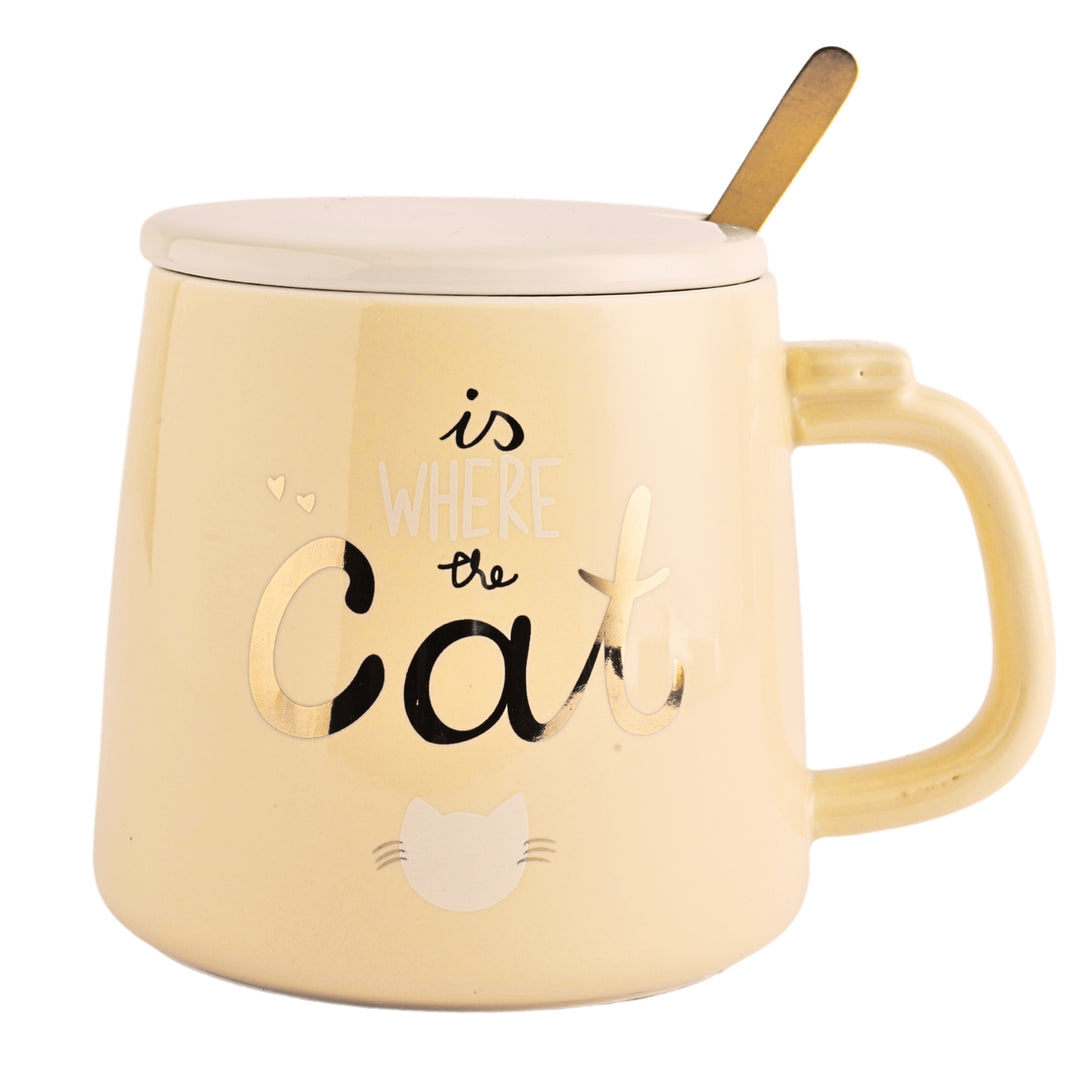 A ceramic mug with a cute cartoon cat printed on the side. The mug is a cream color and has a white ceramic lid.. A golden spoon sits beside the mug.