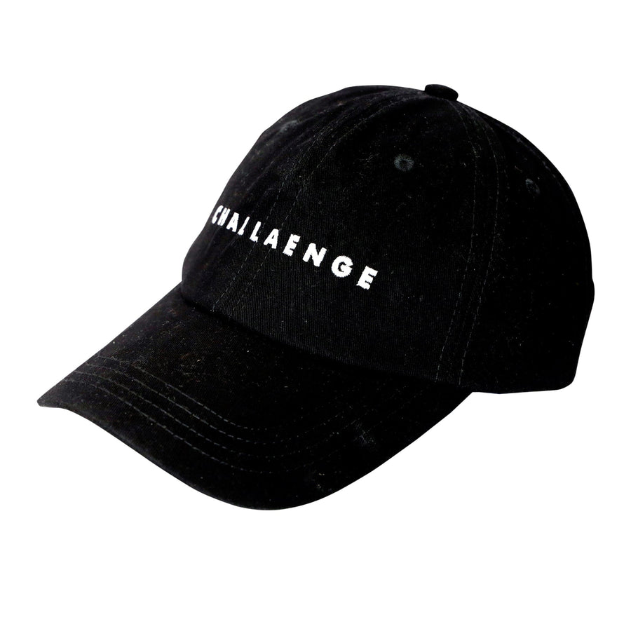 A black cotton baseball cap with a curved brim and an adjustable strap in the back. The front of the cap has the word "Challenge" embroidered on it in a white thread.