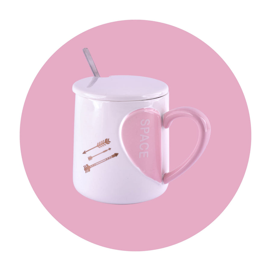 A white ceramic mug with a pink heart-shaped handle and a white ceramic lid with a small handle on top. A white ceramic spoon sits beside the mug.